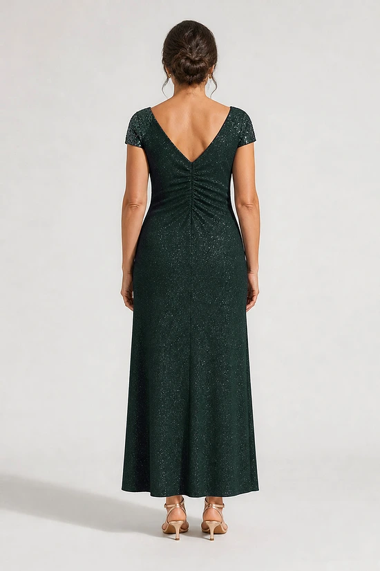 Back view of the Delphine emerald green twist-waist glitter knit gown by Dressology on a regular size model showing the V back and A-line skirt