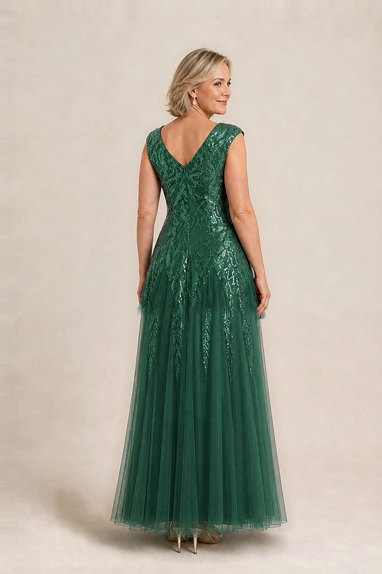Back view of the emerald green glitter embroidered gown showing the V-shaped back and the soft trumpet tulle skirt, worn by a mother of the bride