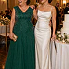 Mother of the bride wearing the emerald green Sylvie glitter embroidered gown by Dressology, laughing with her daughter beside the cake at the reception
