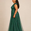 Side view of the emerald green glitter embroidered A-line gown showing the cap sleeve and tulle skirt, worn by a plus-size mother of the bride