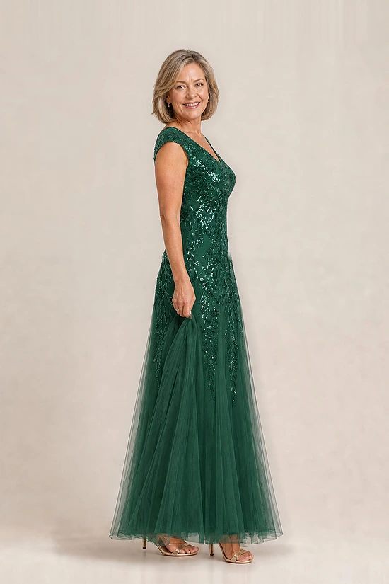 Side view of the emerald green glitter embroidered gown showing the cap sleeve and the soft trumpet tulle skirt, worn by a mother of the bride
